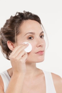 Portrait of woman touching face with cotton pad, studio shot. Photo : Jan Scherders