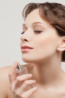Portrait of beautiful young woman spraying perfumes, studio shot. Photo : Jan Scherders