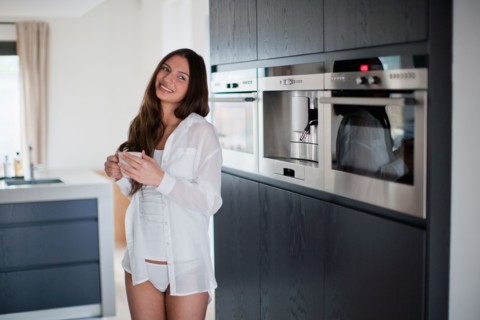 Young woman enjoying coffee in domestic kitchen. Photo : Mark de Leeuw