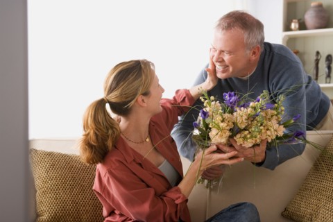 Senior man giving flowers to woman sitting on sofa. Photo : Rob Lewine