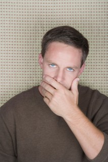 Studio portrait of mature man covering mouth with hand. Photo : Rob Lewine