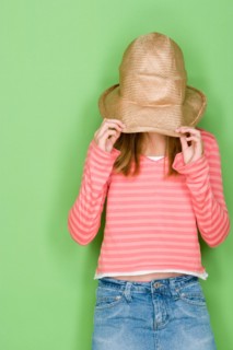Studio portrait of teenage (16-17) girl covering face with hat. Photo : Rob Lewine