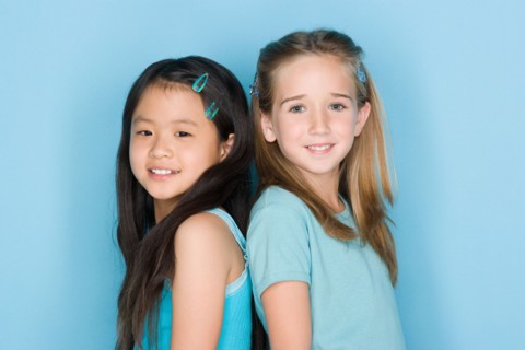 Studio shot portrait of two teenage girls standing back to back, head and shoulders. Photo : Rob