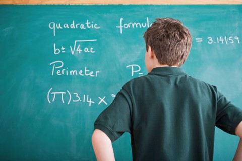 Boy standing in front of blackboard looking at mathematical formula. Photo : Rob Lewine
