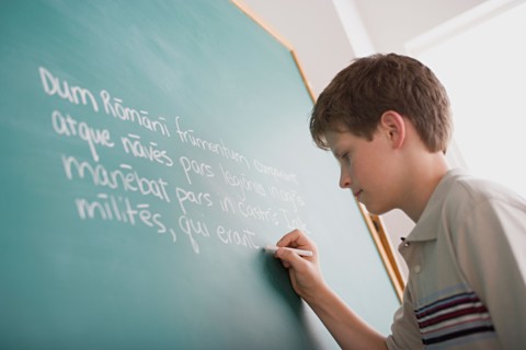 Boy writing Latin text on blackboard. Photo : Rob Lewine