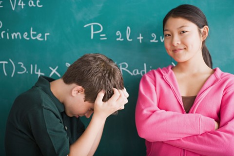 Happy girl and frustrated boy standing in front of blackboard with mathematical formula. Photo :