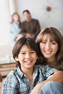 Portrait of brother and sister, parents in background. Photo : Rob Lewine