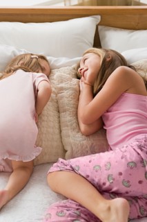 Sisters (8-9, 12-13) lying together on bed. Photo : Rob Lewine