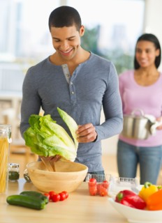 Couple preparing salad in kitchen.