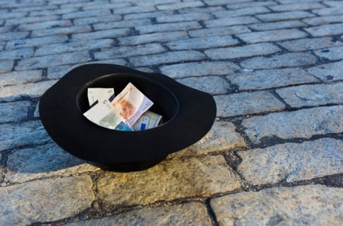 Money in hat on cobblestone street.
