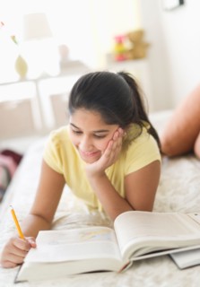 Girl (12-13) lying on bed and studying.