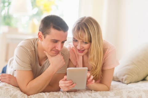 Couple lying on bed and using digital tablet.