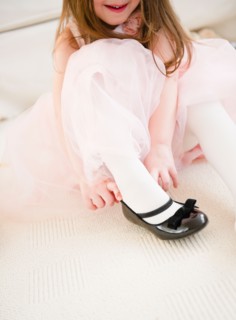 Small girl  (4-5 years)  in tulle dress putting on shoe. Photo : Jamie Grill