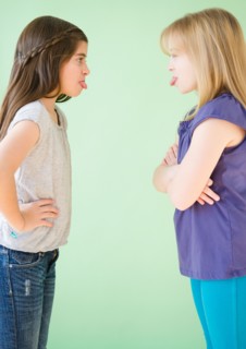 Two girls standing face to face and sticking out tongues. Photo : Jamie Grill