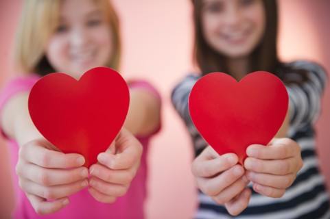 Close up of two girl's hands holding red hearts. Photo : Jamie Grill