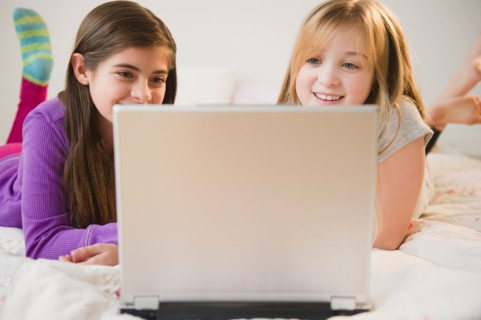 Two girls using laptop on bed. Photo : Jamie Grill