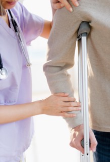 Close up of female doctor helping patient with crutch. Photo : Jamie Grill