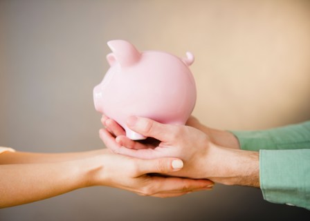 Close up of man's and woman's hands holding piggy bank, studio shot. Photo : Jamie Grill