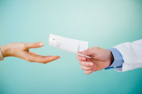Close up of doctor's hand giving prescription to patient,  studio shot. Photo : Jamie Grill