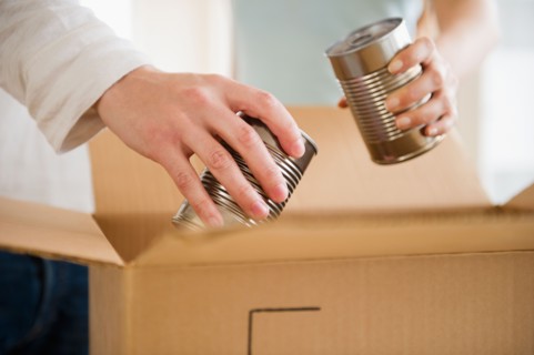 Close up of man's and woman's hands packing cans into box, studio shot. Photo : Jamie Grill