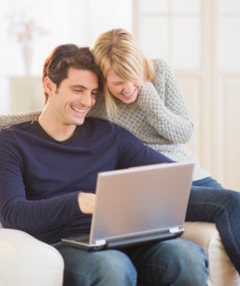 Happy couple sitting together on armchair and using laptop . Photo : Daniel Grill