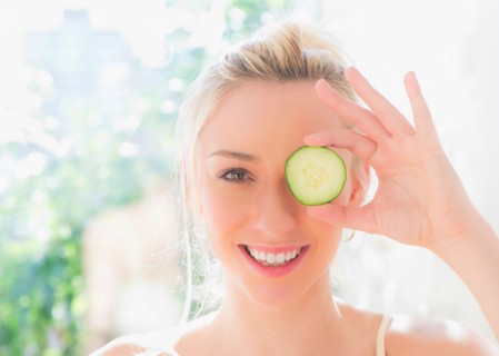 Portrait of smiling young woman covering eye with slice of cucumber. Photo : Daniel Grill