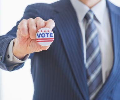 Man wearing suit holding vote pin. Photo : Daniel Grill
