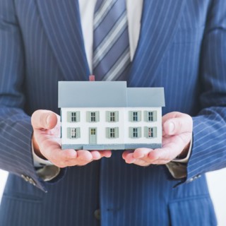 Man wearing suit holding small house model. Photo : Daniel Grill