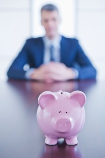 Piggybank on desk, businessman sitting on background. Photo : Daniel Grill