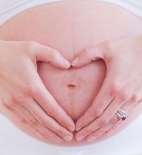 Pregnant woman with hands folded as heart on her belly. Photo : Daniel Grill