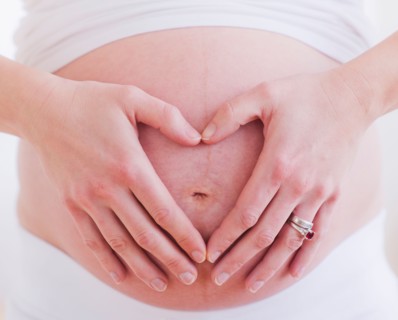 Pregnant woman with hands folded as heart on her belly. Photo : Daniel Grill
