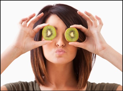 Young woman holding kiwi slices on eyes. Photo : Mike Kemp