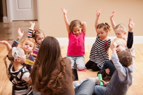 Children (2-3, 4-5) sitting on floor and raising hands. Photo : Mike Kemp