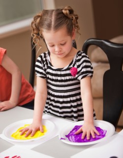 Girl (4-5) holding her hands on plates with paint. Photo : Mike Kemp