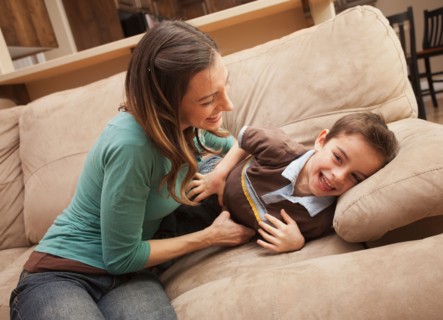 Mother tickling her son (6-7) on couch . Photo : Mike Kemp