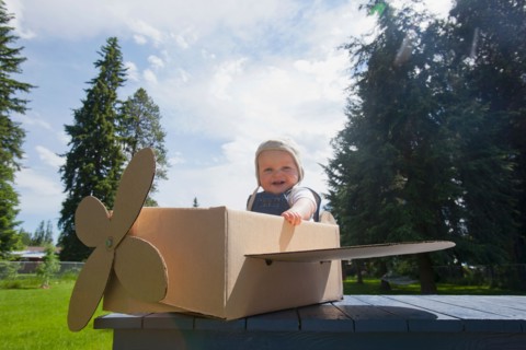 Baby boy (12-17 months) playing inside paper aeroplane made of cardboard box . Photo : Noah Clayton