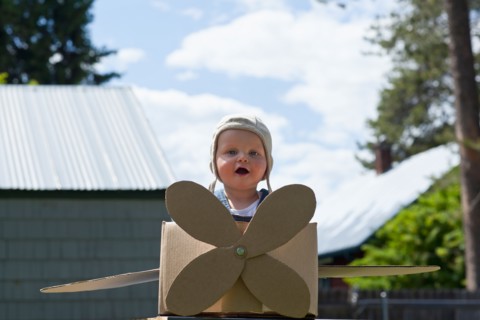 Baby boy (12-17 months) playing inside paper aeroplane made of cardboard box . Photo : Noah Clayton
