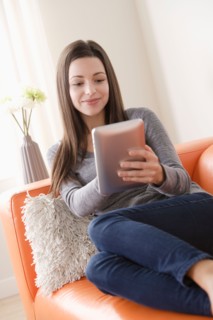 Smiling young woman using digital tablet on sofa. Photo : Rob Lewine