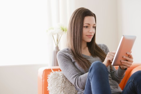 Smiling young woman using digital tablet on sofa. Photo : Rob Lewine