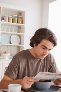 Young man reading newspaper at breakfast. Photo : Rob Lewine