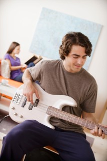 Young man playing electric guitar, young woman in background. Photo : Rob Lewine