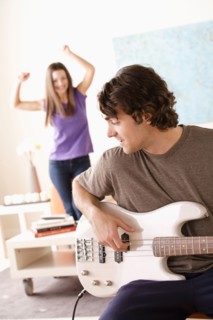 Young man playing electric guitar, young woman dancing in background. Photo : Rob Lewine