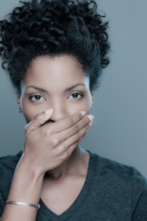 Studio shot of young woman covering lips. Photo : Rob Lewine