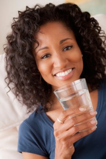 Portrait of smiling woman holding glass of water. Photo : Rob Lewine
