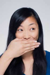 Studio portrait of young woman covering mouth. Photo : Rob Lewine