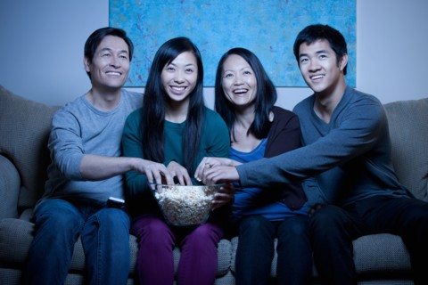 Smiling family watching TV and eating popcorn. Photo : Rob Lewine