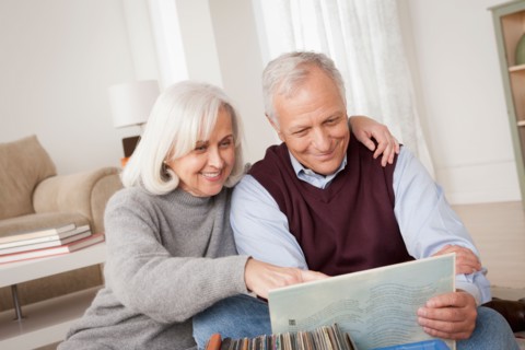 Smiling senior couple looking at vinyl's in living room. Photo : Rob Lewine