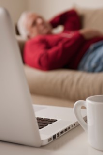 Senior man sleeping on sofa, laptop and mug in foreground. Photo : Rob Lewine