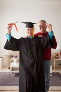 Senior woman wearing graduation gown, happy man in background. Photo : Rob Lewine