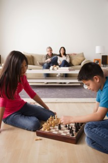 Siblings playing chess game while parents watching from sofa. Photo : Rob Lewine